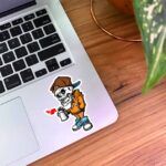 استیکر اسکلت با لباس نارنجی و  کفش آبی درحال گرافیتی زدن